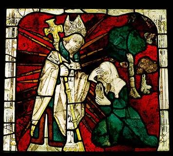 Detail of a medieval glass-stained window of a clergyman healing a blind woman by putting his hand over her eyes. Photo copyright: Historic England